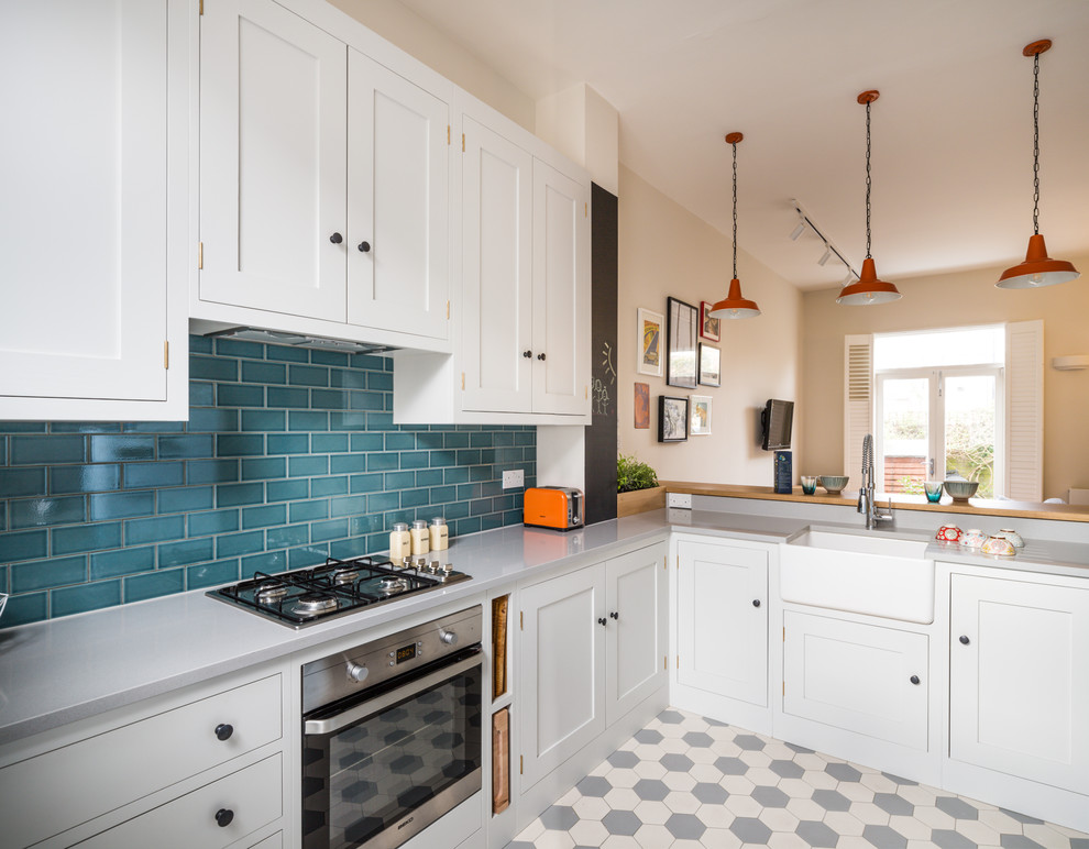 Small contemporary l-shaped open plan kitchen in London with a belfast sink, shaker cabinets, white cabinets, engineered stone countertops, blue splashback, metro tiled splashback, stainless steel appliances, ceramic flooring, a breakfast bar and multi-coloured floors.