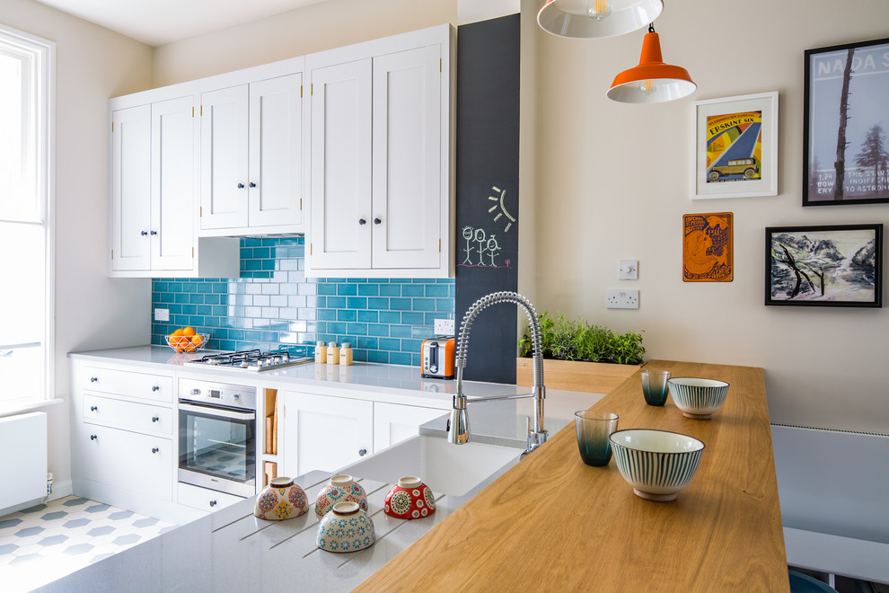 Design ideas for a small contemporary l-shaped open plan kitchen in London with a belfast sink, shaker cabinets, white cabinets, engineered stone countertops, blue splashback, metro tiled splashback, stainless steel appliances, ceramic flooring, a breakfast bar and multi-coloured floors.