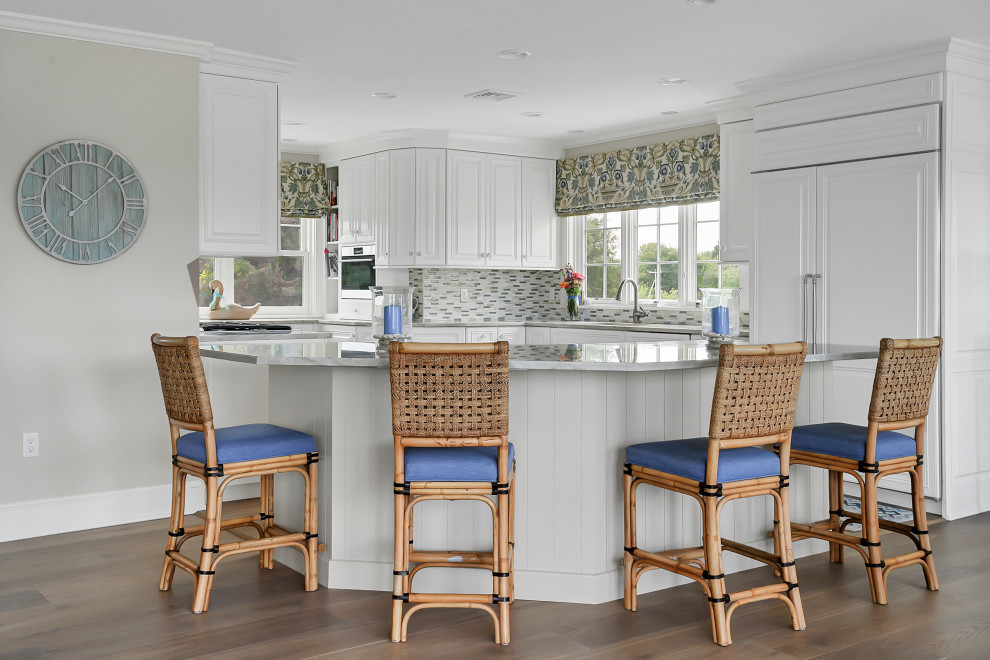 Example of a beach style u-shaped light wood floor kitchen design in Providence with raised-panel cabinets, white cabinets, quartzite countertops, multicolored backsplash, ceramic backsplash, paneled appliances, an island and white countertops