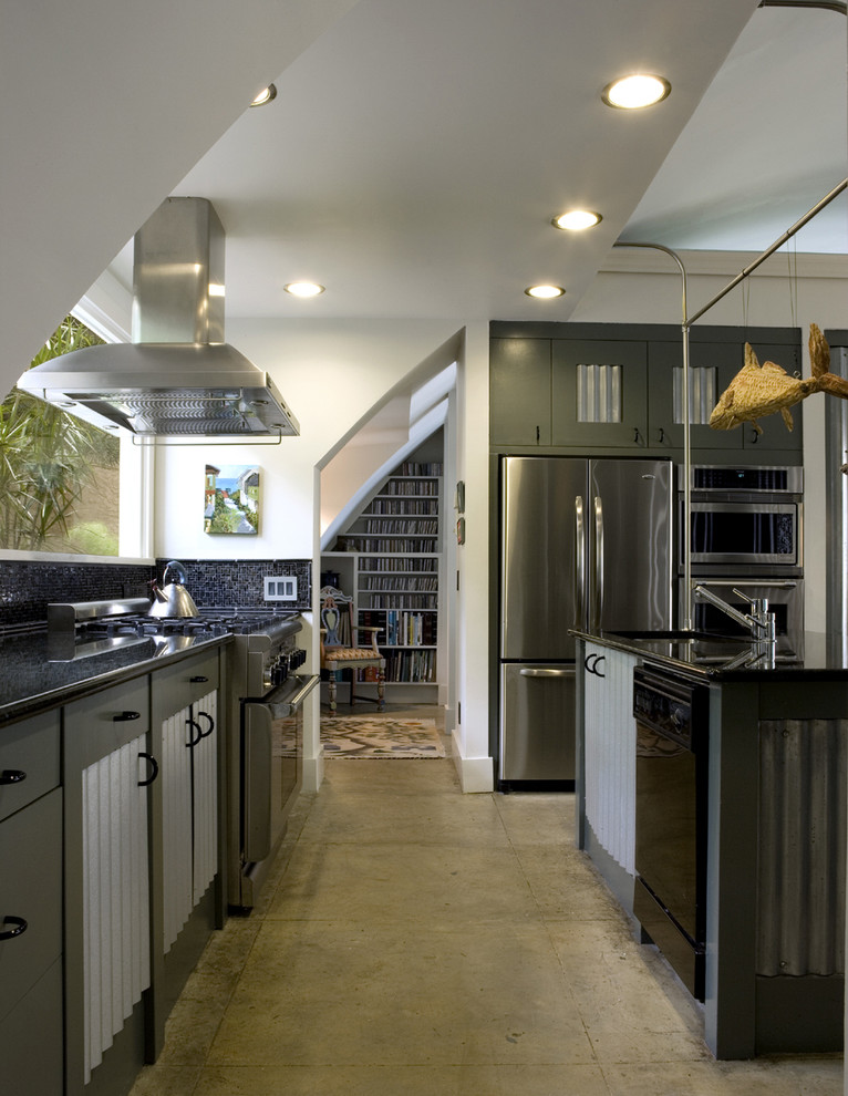 Inredning av ett industriellt mellanstort kök, med rostfria vitvaror, en undermonterad diskho, granitbänkskiva, svart stänkskydd, stänkskydd i glaskakel, betonggolv, en köksö och grå skåp