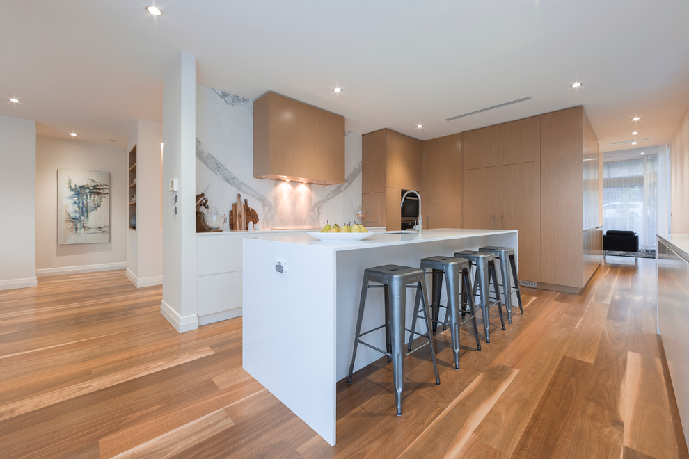 Design ideas for a contemporary l-shaped kitchen pantry in Canberra - Queanbeyan with a single-bowl sink, flat-panel cabinets, white cabinets, engineered stone countertops, white splashback, stone slab splashback, black appliances, an island and medium hardwood flooring.