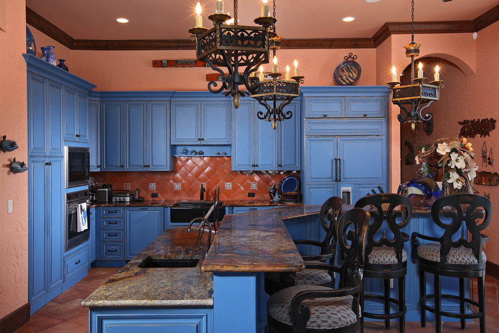 マイアミにある地中海スタイルのおしゃれなキッチン (ドロップインシンク、レイズドパネル扉のキャビネット、青いキャビネット、御影石カウンター、オレンジのキッチンパネル、セラミックタイルのキッチンパネル、シルバーの調理設備、セラミックタイルの床) の写真
