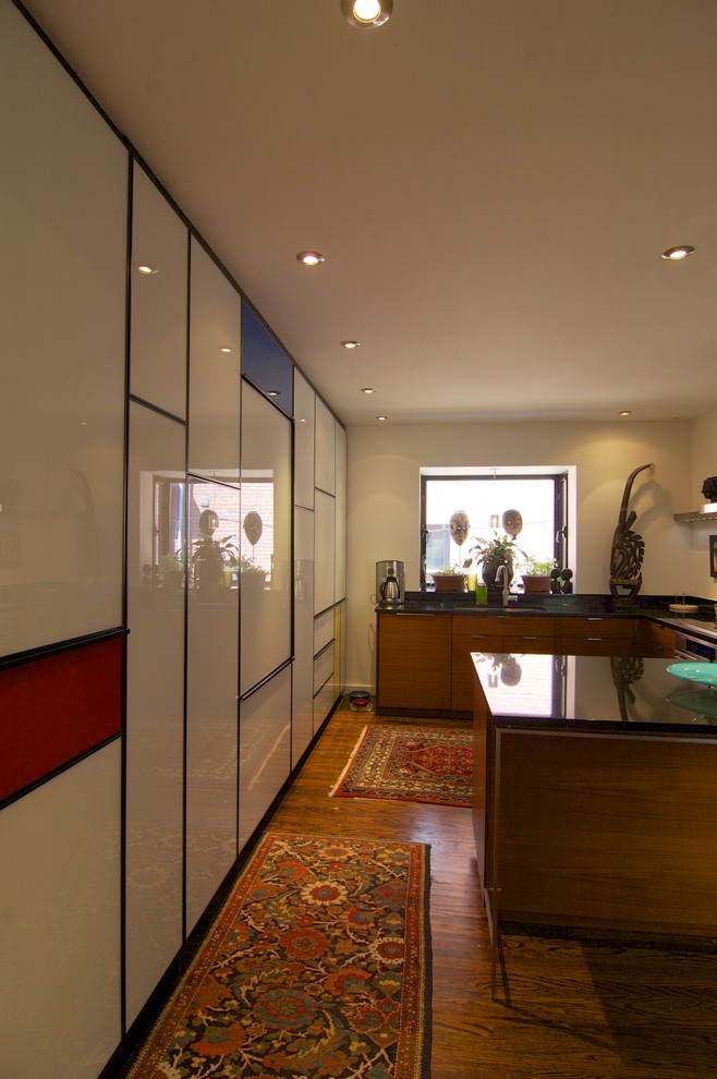 Inredning av ett modernt kök, med en undermonterad diskho, luckor med glaspanel, vita skåp, granitbänkskiva, vitt stänkskydd, färgglada vitvaror och mörkt trägolv