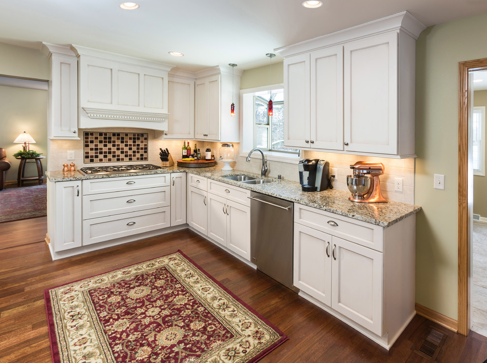 This is an example of a large traditional l-shaped kitchen/diner in Milwaukee with a submerged sink, recessed-panel cabinets, white cabinets, granite worktops, white splashback, metro tiled splashback, stainless steel appliances and medium hardwood flooring.