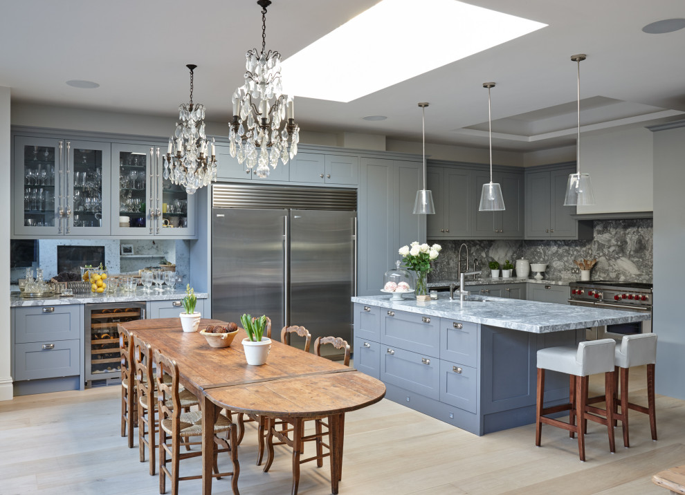 Example of a large transitional u-shaped light wood floor and beige floor eat-in kitchen design in London with shaker cabinets, gray cabinets, gray backsplash, stone slab backsplash, an island and gray countertops