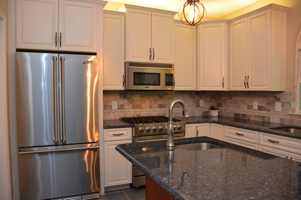 Klassisk inredning av ett mellanstort kök, med en undermonterad diskho, luckor med infälld panel, vita skåp, bänkskiva i kvarts, grått stänkskydd, stänkskydd i keramik, rostfria vitvaror, en köksö och grått golv