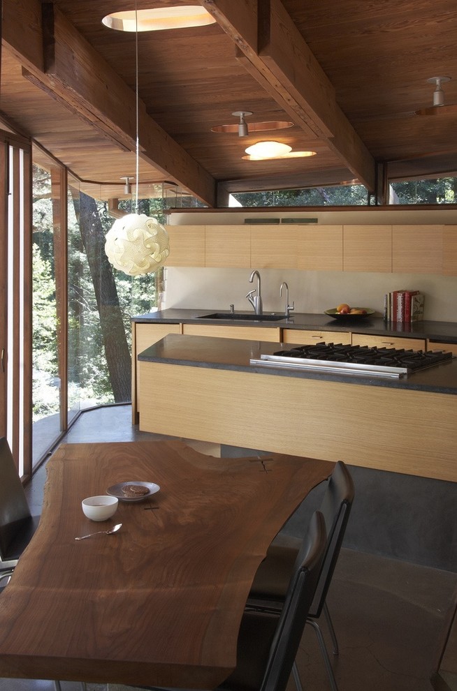 Cette image montre une cuisine américaine minimaliste en bois clair avec un placard à porte plane, un plan de travail en granite et un électroménager en acier inoxydable.