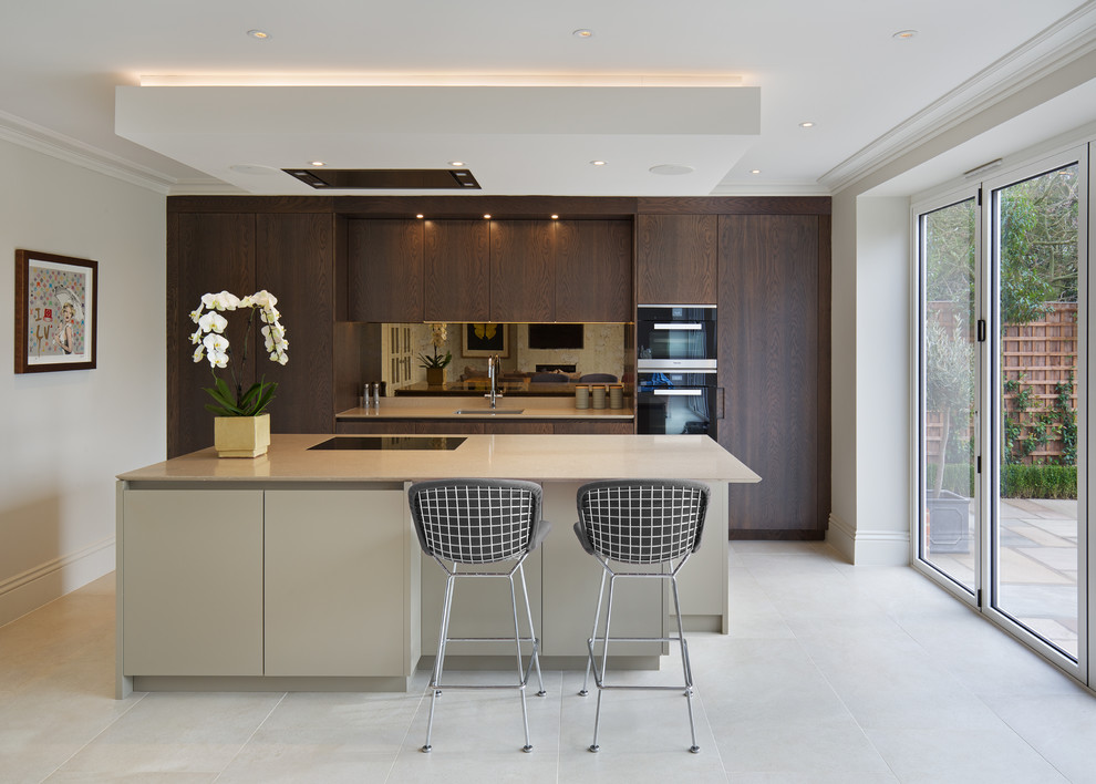 This is an example of a large contemporary galley open plan kitchen in Hertfordshire with a submerged sink, flat-panel cabinets, dark wood cabinets, quartz worktops, metallic splashback, mirror splashback, black appliances, porcelain flooring, an island and white floors.