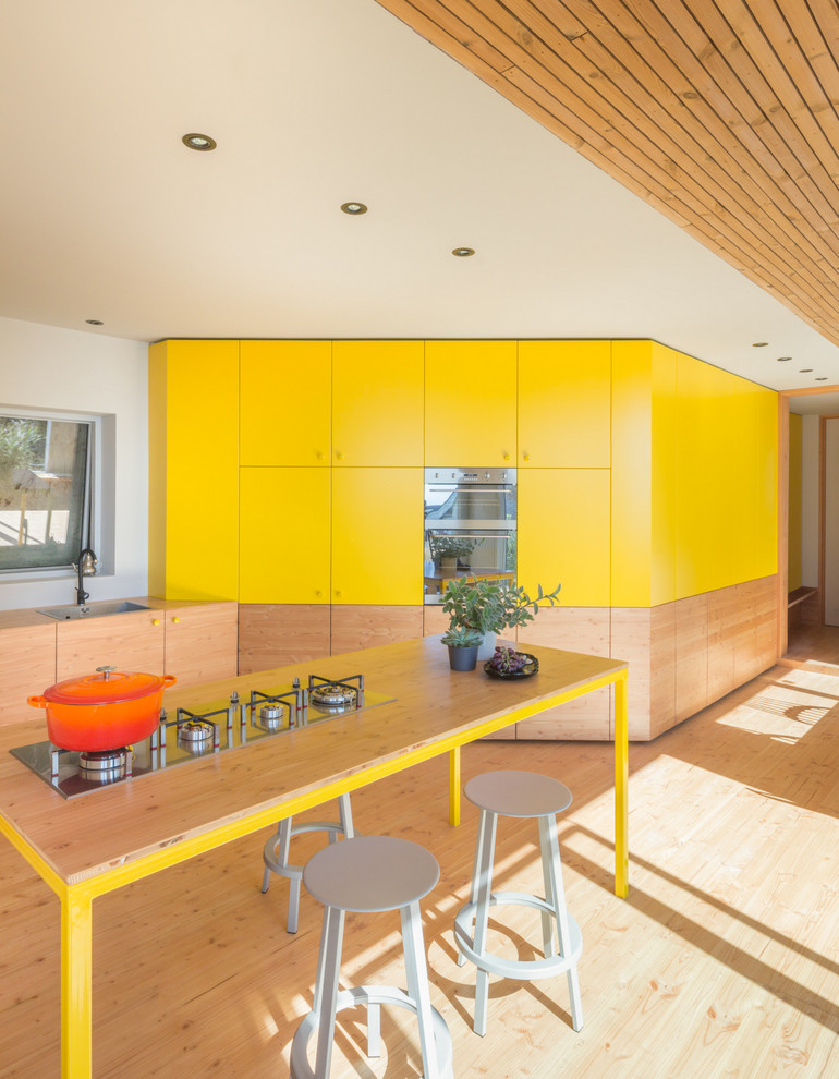 Inspiration for a large contemporary l-shaped kitchen/diner in London with a single-bowl sink, flat-panel cabinets, yellow cabinets, wood worktops, integrated appliances, light hardwood flooring, an island, beige floors and beige worktops.