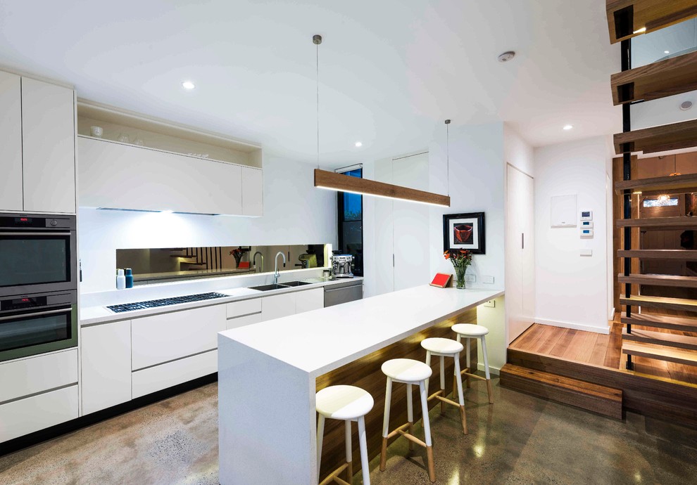 Inspiration for a medium sized contemporary single-wall open plan kitchen in Melbourne with concrete flooring, a double-bowl sink, flat-panel cabinets, white cabinets, granite worktops, metallic splashback, mirror splashback, black appliances and an island.