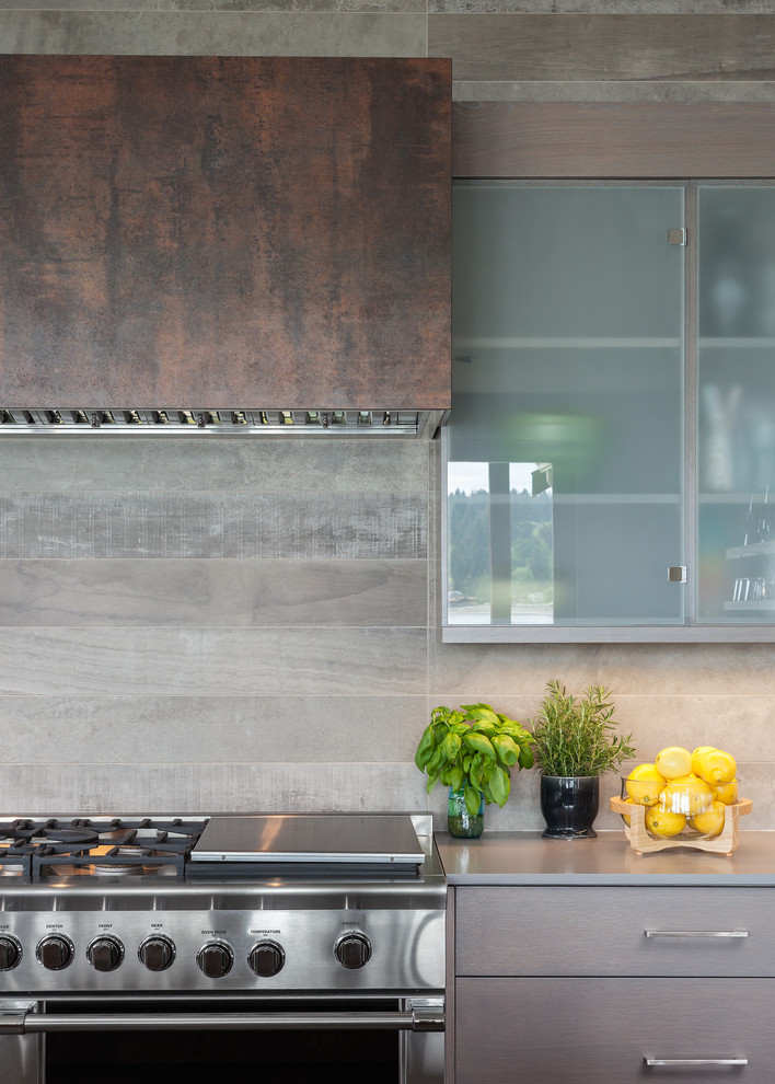 Medium sized coastal u-shaped kitchen/diner in Seattle with a built-in sink, flat-panel cabinets, grey cabinets, tile countertops, grey splashback, ceramic splashback, stainless steel appliances, concrete flooring, an island and brown floors.