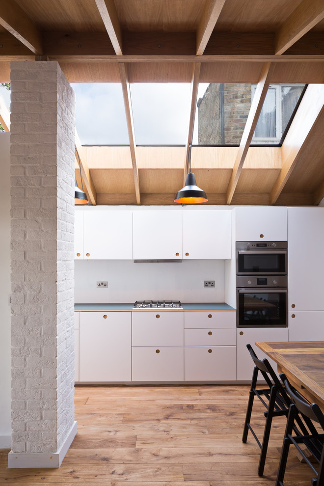 Medium sized scandi single-wall enclosed kitchen in London with flat-panel cabinets, white cabinets, stainless steel appliances, white splashback, medium hardwood flooring and brown floors.