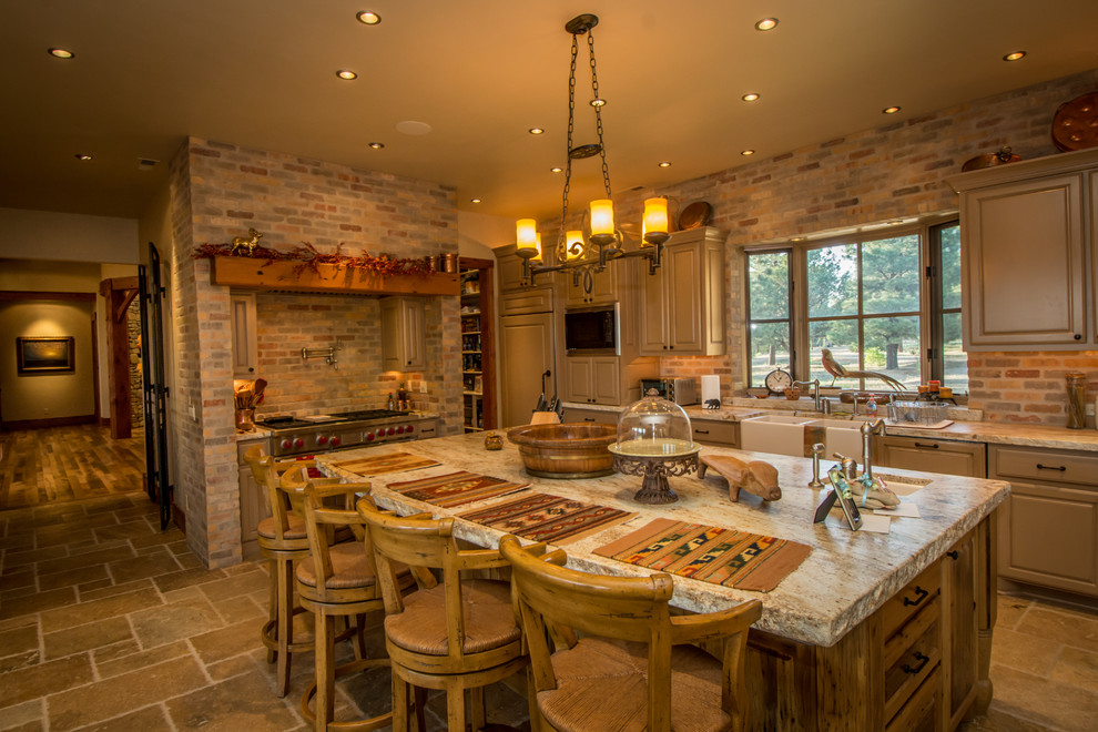 Inspiration for an expansive rustic kitchen/diner in Denver with a belfast sink, distressed cabinets, granite worktops, stainless steel appliances, travertine flooring, an island, louvered cabinets, red splashback and stone tiled splashback.
