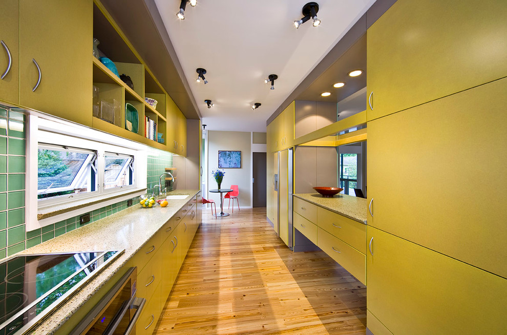 アトランタにある広いコンテンポラリースタイルのおしゃれなキッチン (フラットパネル扉のキャビネット、黄色いキャビネット、緑のキッチンパネル、シルバーの調理設備、アンダーカウンターシンク、再生ガラスカウンター、ガラスタイルのキッチンパネル、淡色無垢フローリング、茶色い床) の写真