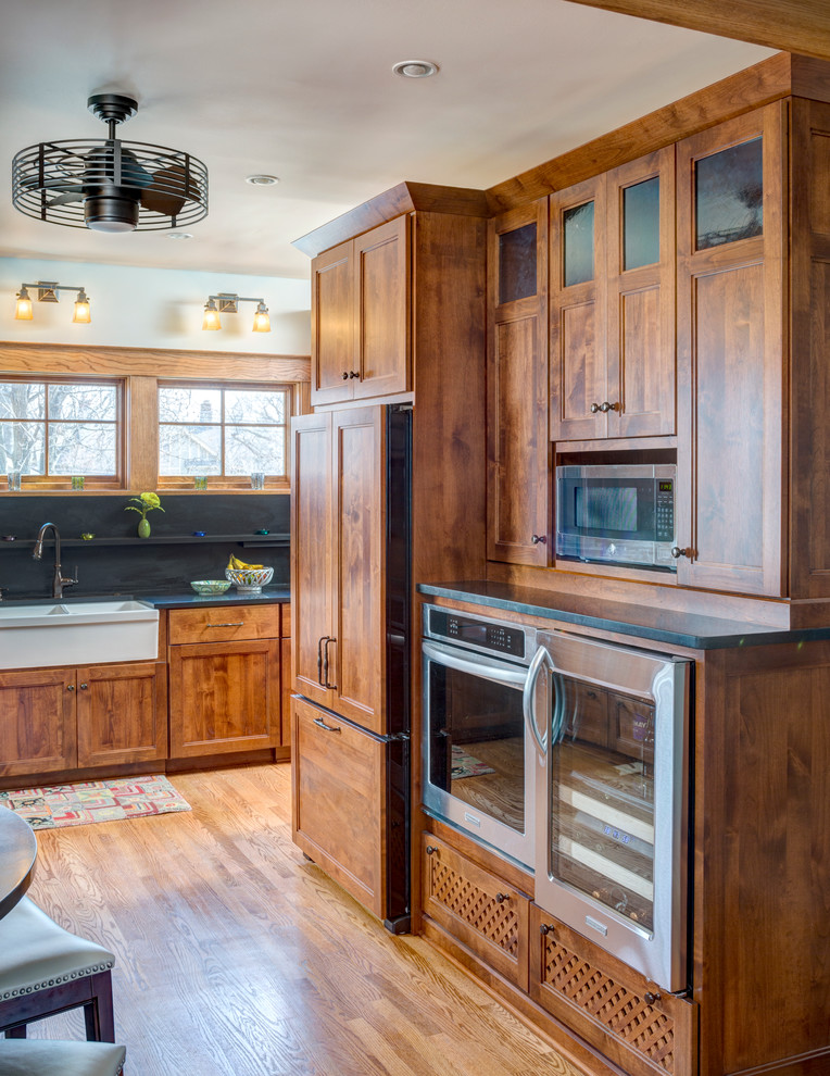 Inspiration for a small craftsman galley medium tone wood floor and brown floor eat-in kitchen remodel in Kansas City with a farmhouse sink, shaker cabinets, medium tone wood cabinets, granite countertops, black backsplash, stone slab backsplash, stainless steel appliances and no island