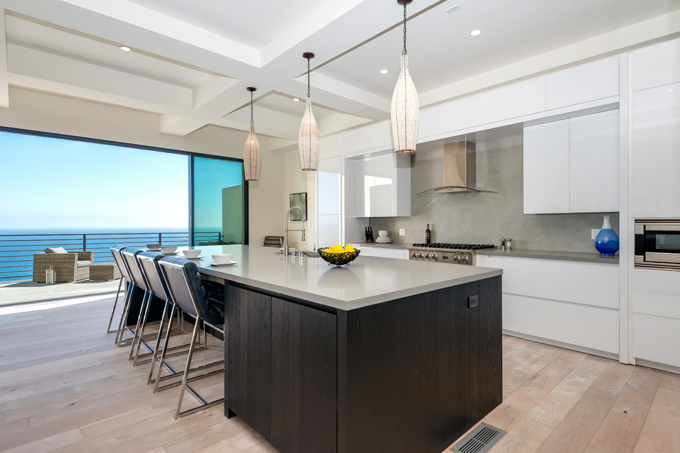 Moderne Küche mit flächenbündigen Schrankfronten, weißen Schränken, Küchenrückwand in Grau, Küchengeräten aus Edelstahl, hellem Holzboden, Kücheninsel und grauer Arbeitsplatte in Los Angeles
