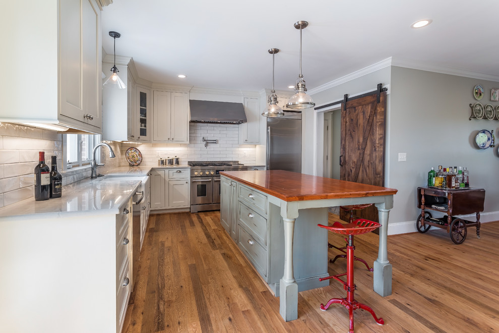 Inspiration for a country l-shaped light wood floor open concept kitchen remodel in DC Metro with a farmhouse sink, shaker cabinets, white cabinets, quartzite countertops, white backsplash, ceramic backsplash, stainless steel appliances and an island