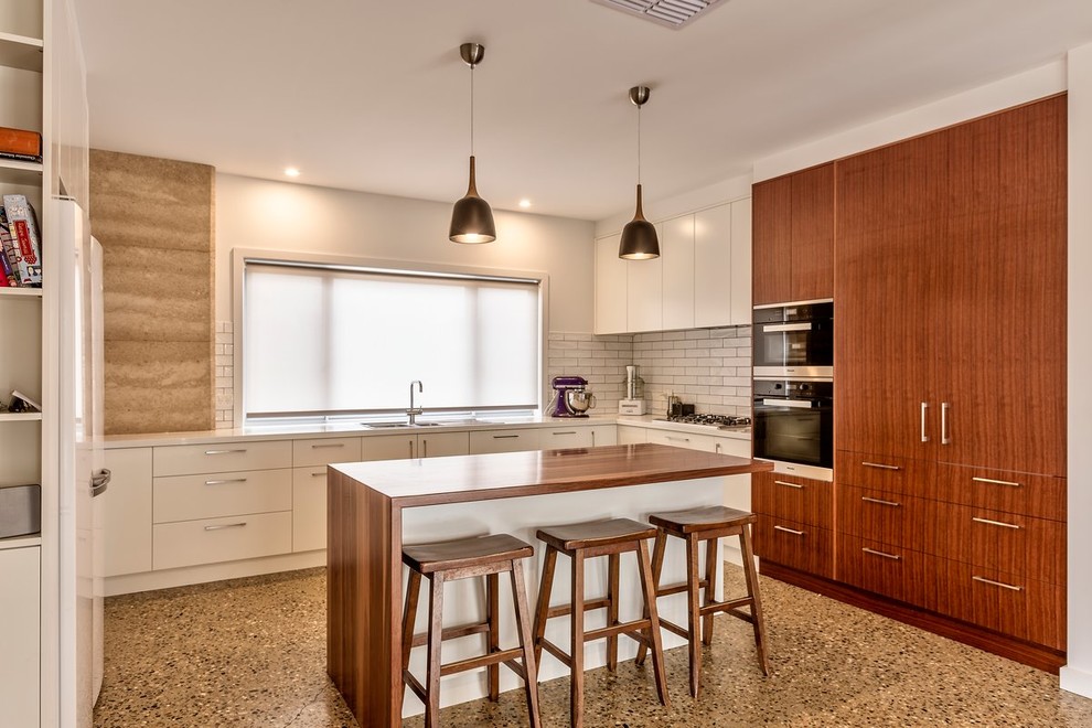 Eat-in kitchen - mid-sized contemporary u-shaped concrete floor eat-in kitchen idea in Melbourne with a double-bowl sink, flat-panel cabinets, wood countertops, white backsplash, subway tile backsplash, stainless steel appliances and an island
