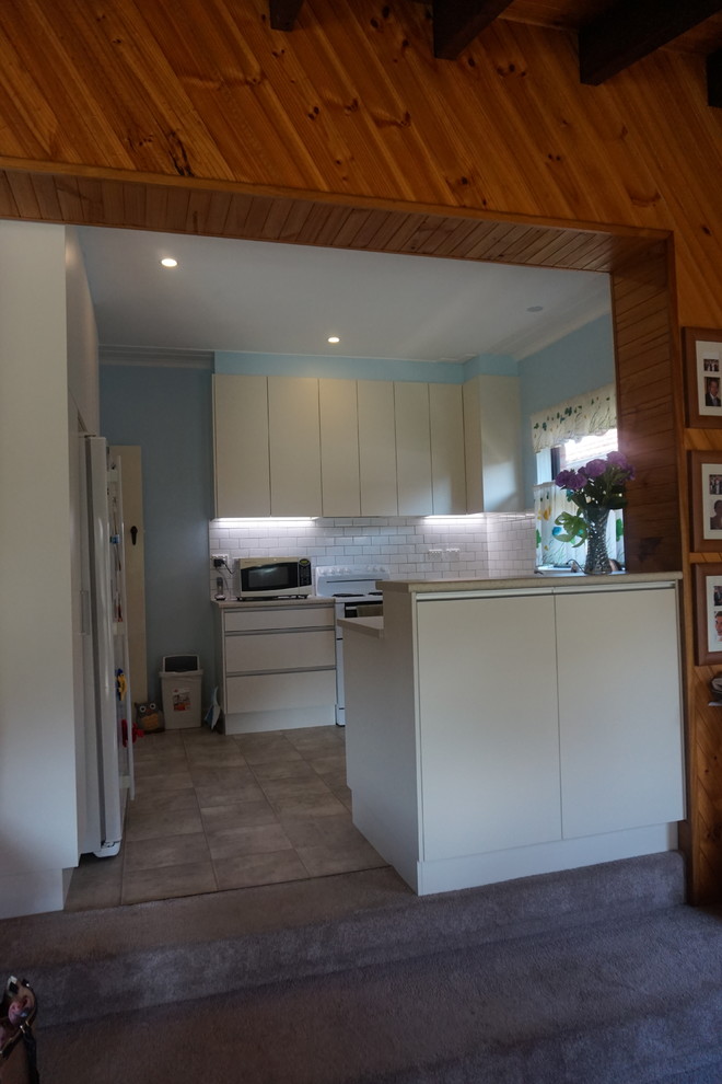Large modern u-shaped open plan kitchen in Sydney with a built-in sink, white cabinets, laminate countertops, white splashback, metro tiled splashback, white appliances and vinyl flooring.