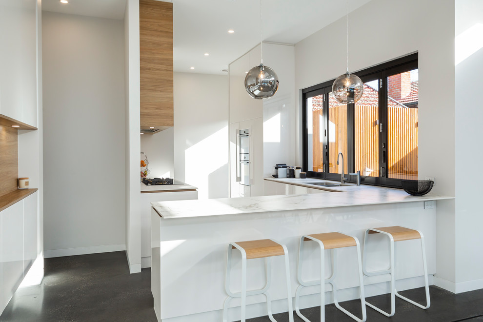 Offene Moderne Küche mit Unterbauwaschbecken, flächenbündigen Schrankfronten, weißen Schränken, Halbinsel, grauem Boden und weißer Arbeitsplatte in Adelaide