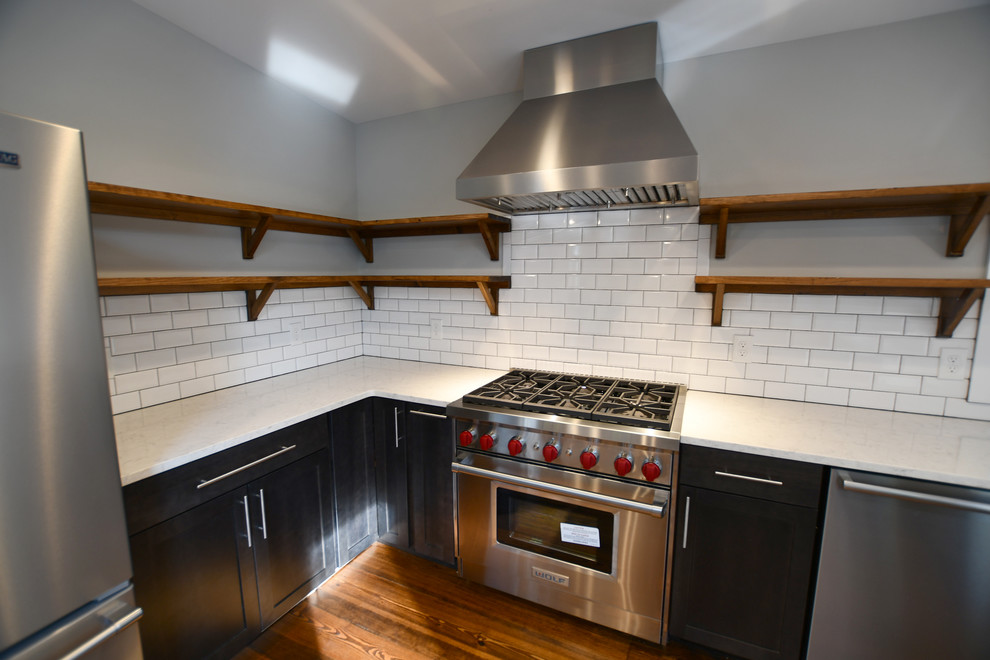 Inspiration for a large 1960s u-shaped medium tone wood floor and brown floor open concept kitchen remodel in New York with shaker cabinets, black cabinets, white backsplash, no island, white countertops, quartz countertops, subway tile backsplash and stainless steel appliances
