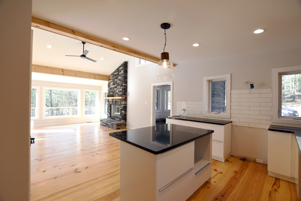 Example of a mid-sized 1960s u-shaped light wood floor and brown floor open concept kitchen design in New York with an undermount sink, flat-panel cabinets, white cabinets, quartz countertops, white backsplash, ceramic backsplash, an island and black countertops