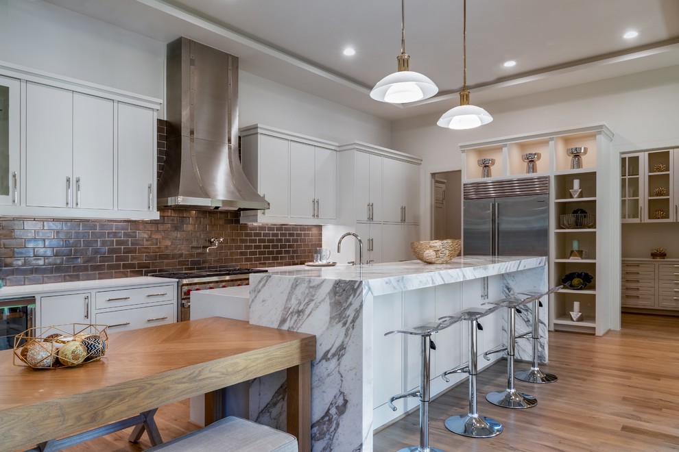 Medium sized classic l-shaped open plan kitchen in Houston with flat-panel cabinets, white cabinets, brown splashback, metro tiled splashback, stainless steel appliances, an island, a submerged sink, composite countertops, light hardwood flooring, beige floors and white worktops.