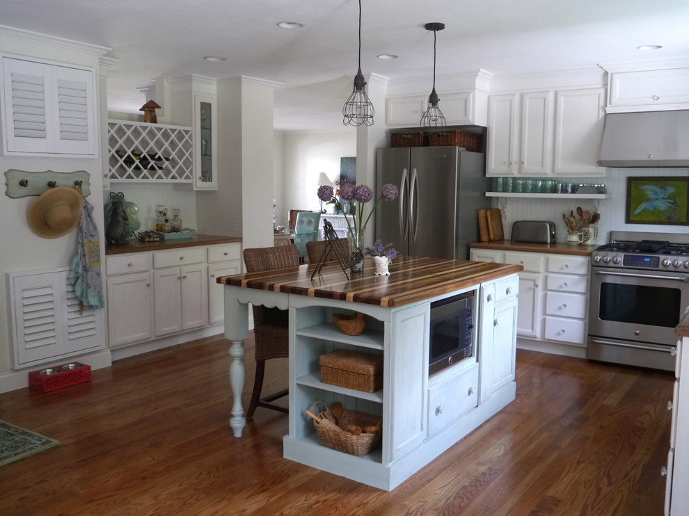 Mid-sized country u-shaped medium tone wood floor open concept kitchen photo in DC Metro with a farmhouse sink, recessed-panel cabinets, distressed cabinets, wood countertops, white backsplash, stainless steel appliances and an island