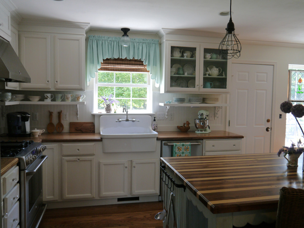 Medium sized farmhouse u-shaped open plan kitchen in DC Metro with a belfast sink, recessed-panel cabinets, distressed cabinets, wood worktops, white splashback, stainless steel appliances, medium hardwood flooring and an island.