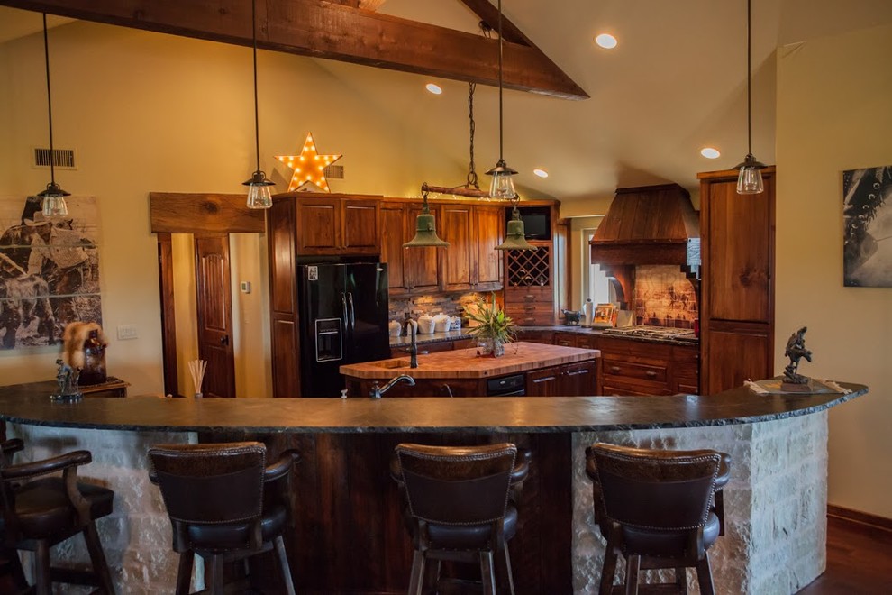 This is an example of a large l-shaped kitchen/diner in Dallas with a submerged sink, raised-panel cabinets, medium wood cabinets, stone tiled splashback, black appliances, dark hardwood flooring, multiple islands and brown floors.