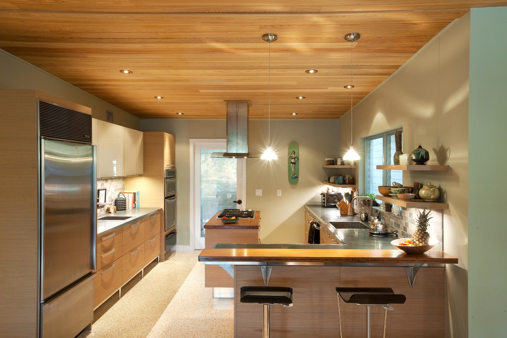 На фото: кухня в современном стиле с монолитной мойкой, плоскими фасадами, светлыми деревянными фасадами, столешницей из нержавеющей стали, серым фартуком и техникой из нержавеющей стали