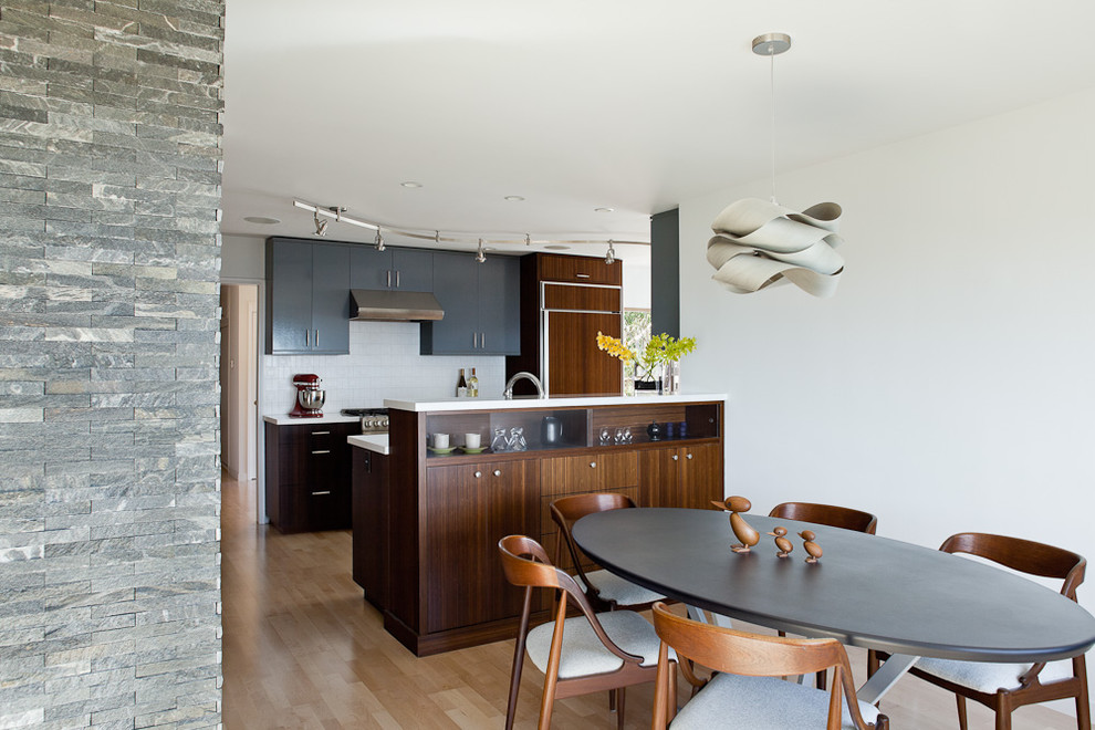 Modern inredning av ett kök, med släta luckor, svarta skåp, bänkskiva i kvarts, vitt stänkskydd, stänkskydd i porslinskakel, rostfria vitvaror och ljust trägolv