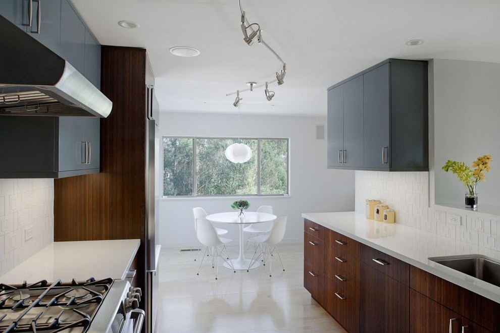 Inspiration for a modern galley kitchen in San Francisco with flat-panel cabinets, dark wood cabinets, white splashback, a submerged sink, porcelain splashback, stainless steel appliances and light hardwood flooring.