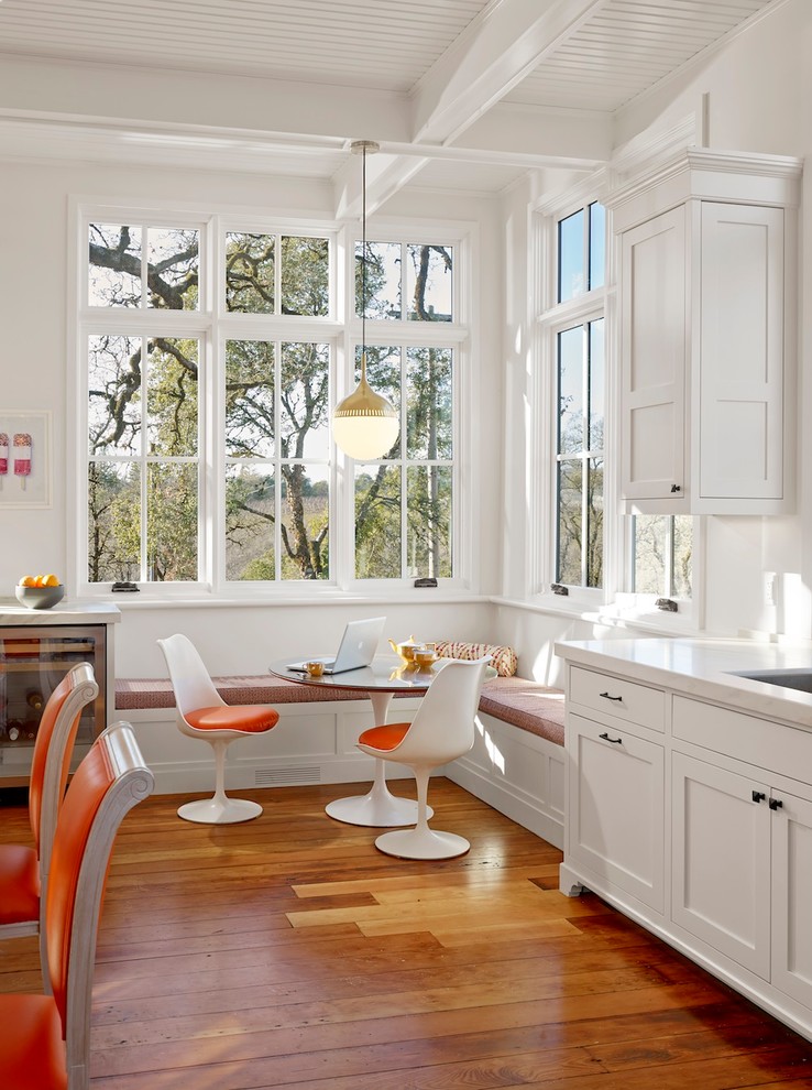 На фото: кухня в стиле кантри с обеденным столом, фасадами в стиле шейкер, белыми фасадами и паркетным полом среднего тона с