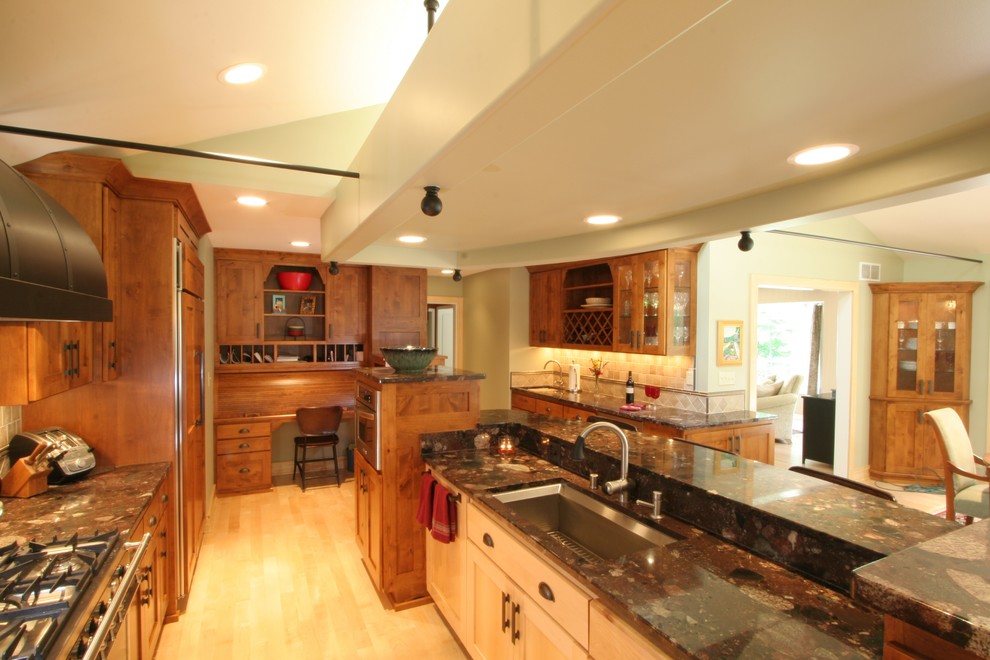 Cette image montre une cuisine américaine traditionnelle en bois brun avec un évier encastré, un placard à porte plane, un plan de travail en granite, une crédence beige, une crédence en carreau de porcelaine et un électroménager noir.