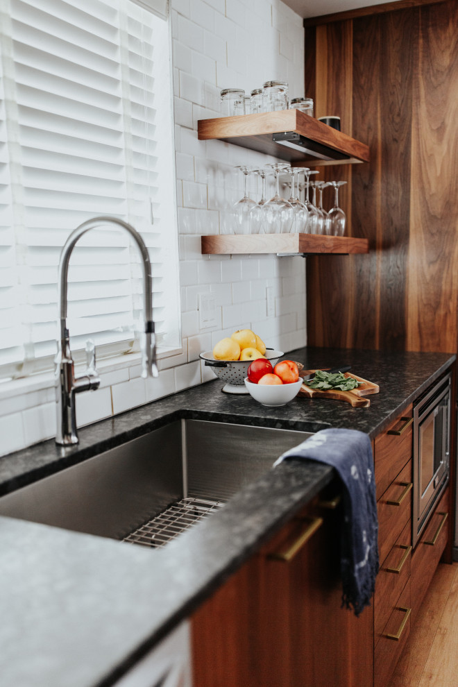 Immagine di una cucina moderna di medie dimensioni con lavello sottopiano, ante lisce, ante in legno scuro, top in granito, paraspruzzi bianco, paraspruzzi con piastrelle in ceramica, elettrodomestici in acciaio inossidabile, pavimento in laminato, pavimento marrone e top nero