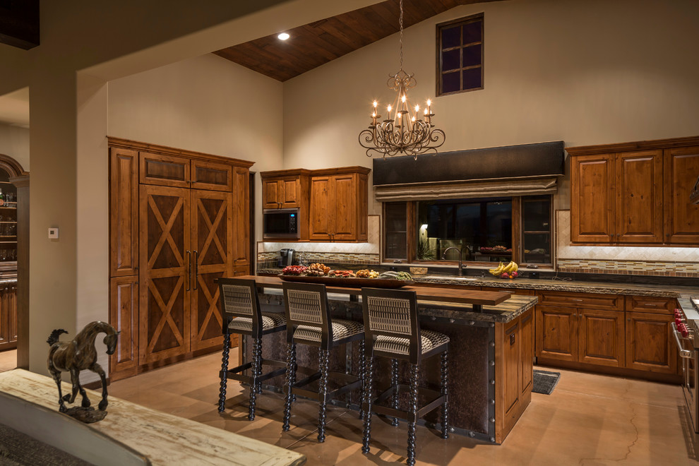 Example of a large southwest l-shaped concrete floor and brown floor eat-in kitchen design in Phoenix with raised-panel cabinets, medium tone wood cabinets, paneled appliances, an island, an undermount sink, granite countertops, multicolored backsplash and stone tile backsplash