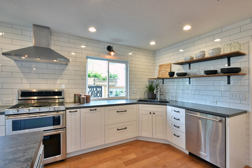 Inspiration for a large urban u-shaped open plan kitchen in Tampa with shaker cabinets, white cabinets, engineered stone countertops, white splashback, metro tiled splashback, stainless steel appliances, light hardwood flooring, an island, brown floors and a double-bowl sink.
