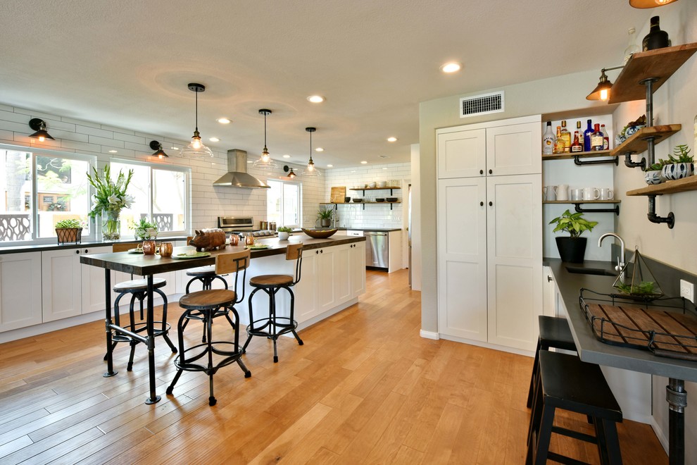 Example of a large urban u-shaped light wood floor and brown floor open concept kitchen design in Tampa with a single-bowl sink, shaker cabinets, white cabinets, quartz countertops, white backsplash, subway tile backsplash, stainless steel appliances and an island