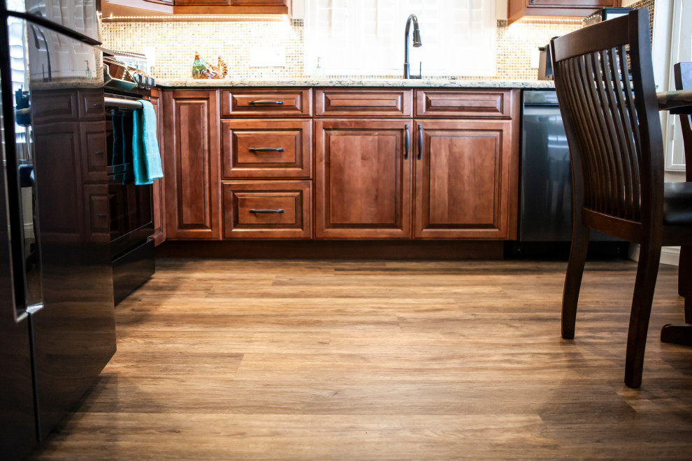 Foto på ett mellanstort vintage brun kök, med en dubbel diskho, luckor med upphöjd panel, skåp i mellenmörkt trä, bänkskiva i kvarts, flerfärgad stänkskydd, stänkskydd i glaskakel, svarta vitvaror och laminatgolv