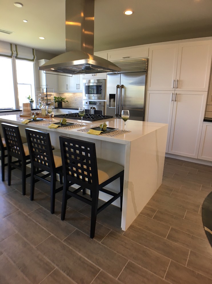 Inspiration for a large transitional l-shaped light wood floor eat-in kitchen remodel in Los Angeles with an undermount sink, shaker cabinets, white cabinets, marble countertops, white backsplash, matchstick tile backsplash, stainless steel appliances and an island
