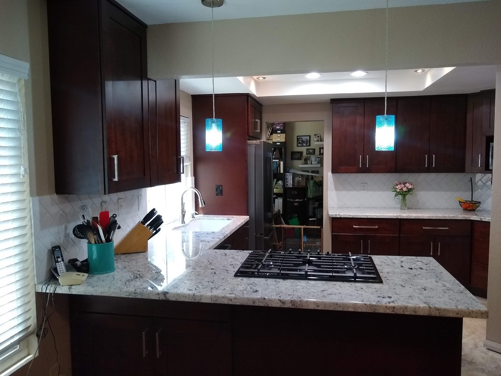 This is an example of a medium sized traditional l-shaped kitchen/diner in San Diego with a double-bowl sink, shaker cabinets, dark wood cabinets, granite worktops, white splashback, glass tiled splashback, stainless steel appliances, light hardwood flooring, multi-coloured floors and white worktops.
