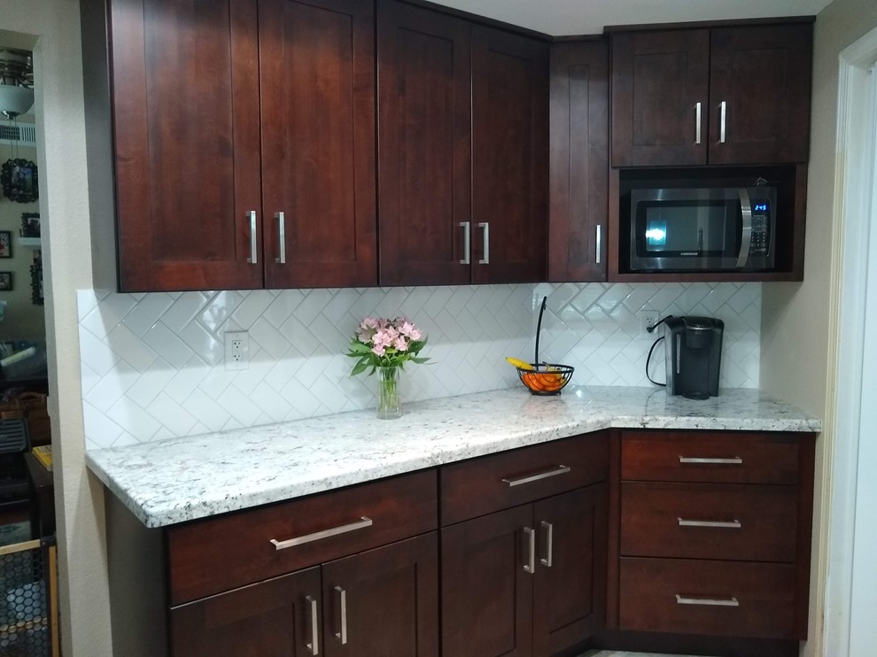 Example of a mid-sized classic l-shaped light wood floor and multicolored floor eat-in kitchen design in San Diego with a double-bowl sink, shaker cabinets, dark wood cabinets, granite countertops, white backsplash, glass tile backsplash, stainless steel appliances and white countertops