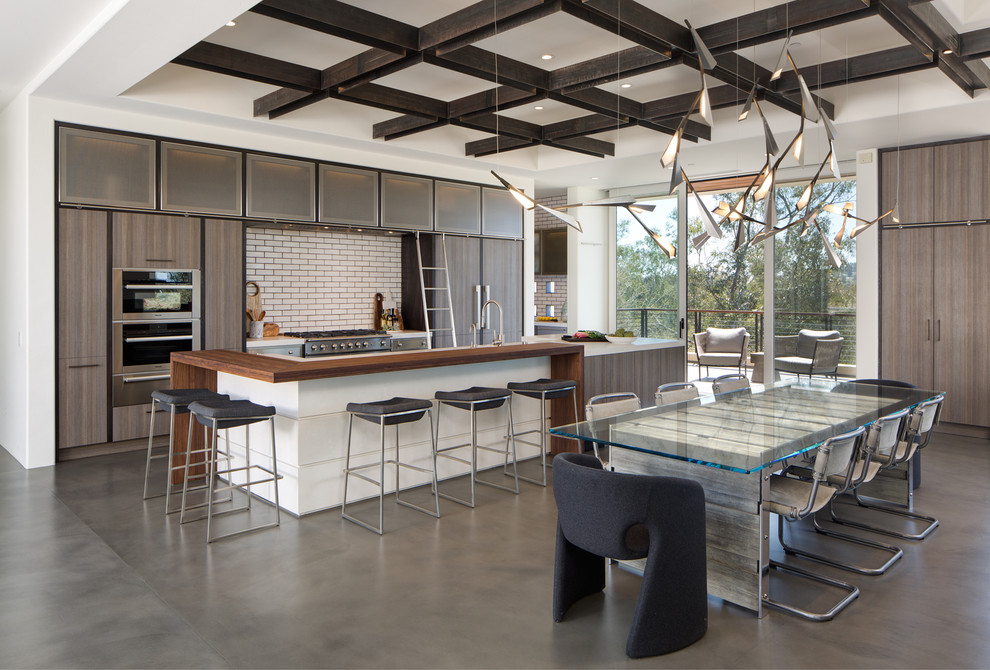 Example of a trendy galley concrete floor and gray floor open concept kitchen design in San Diego with a double-bowl sink, flat-panel cabinets, medium tone wood cabinets, quartz countertops, white backsplash, stainless steel appliances, an island and ceramic backsplash