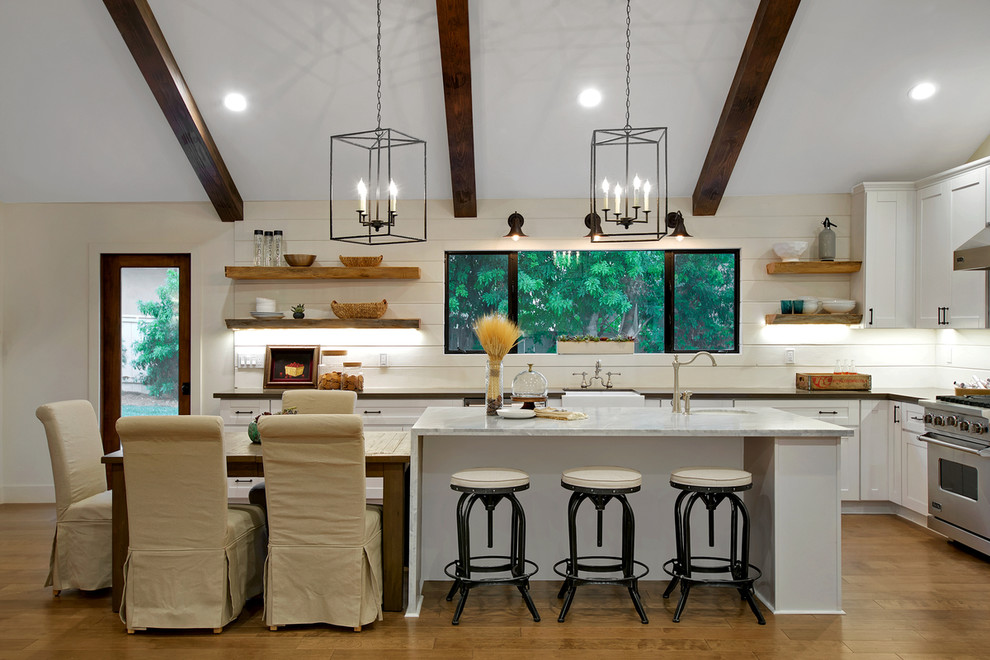 Lantlig inredning av ett kök, med en rustik diskho, skåp i shakerstil, vita skåp, vitt stänkskydd, rostfria vitvaror, mellanmörkt trägolv och en köksö
