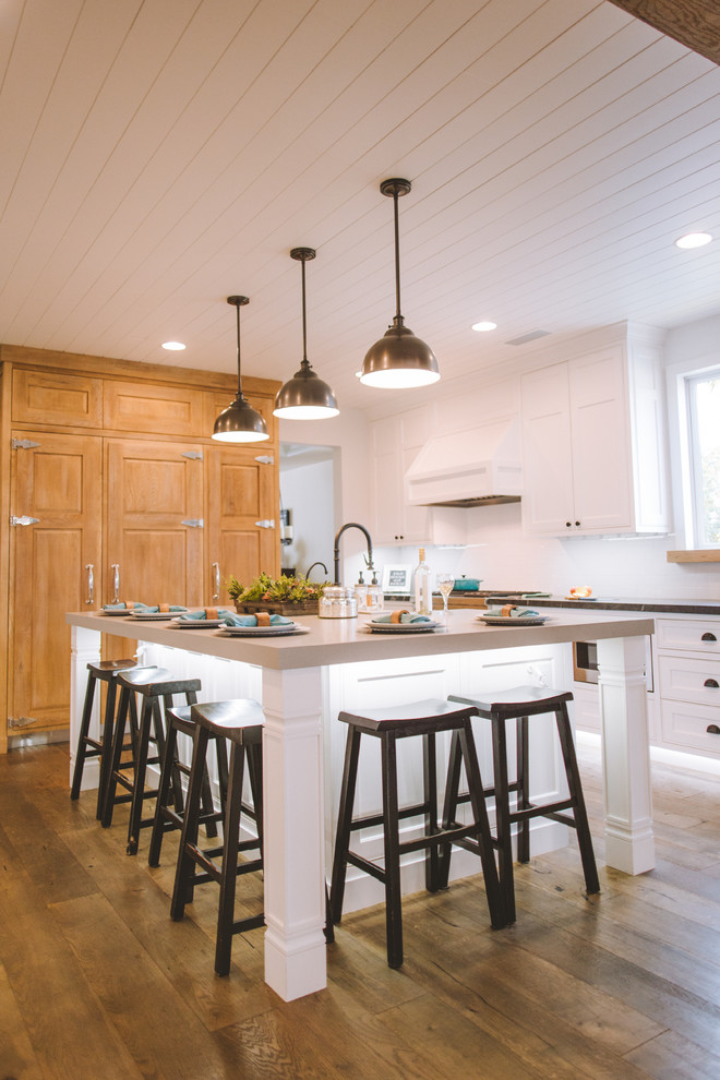 Inspiration for a large country u-shaped open plan kitchen in Orange County with a belfast sink, shaker cabinets, white cabinets, white splashback, metro tiled splashback, stainless steel appliances, medium hardwood flooring, an island and brown floors.