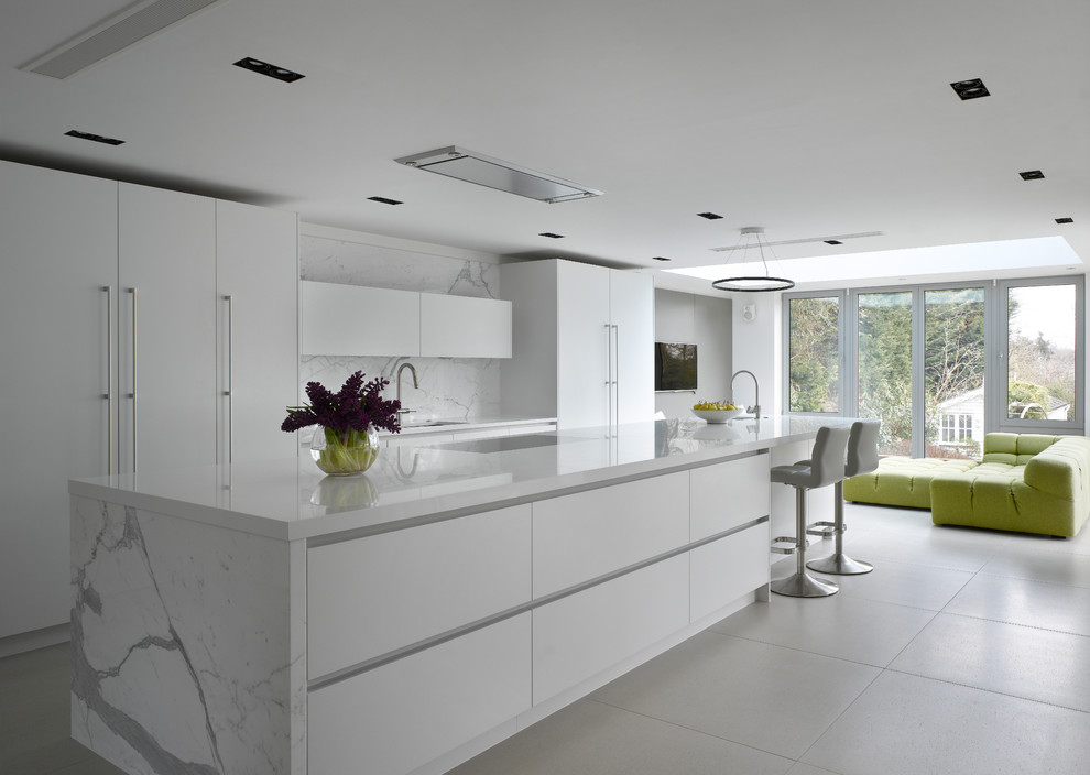 Design ideas for a large contemporary galley open plan kitchen in London with flat-panel cabinets, white cabinets, composite countertops, white splashback, marble splashback, integrated appliances, an island, white worktops, a submerged sink and grey floors.