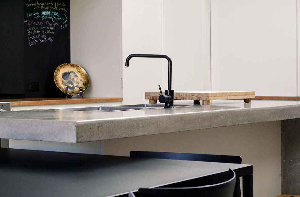 Foto di una cucina design di medie dimensioni con lavello a doppia vasca, ante bianche, top in cemento, paraspruzzi nero, paraspruzzi con lastra di vetro, elettrodomestici da incasso e pavimento in cemento