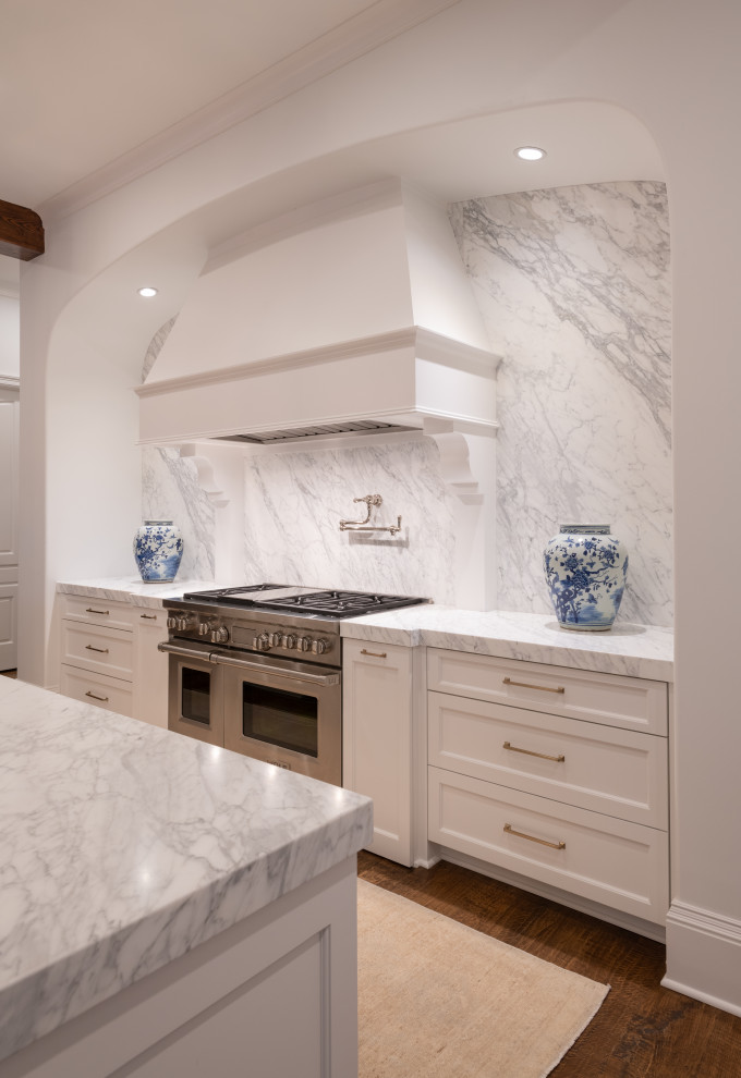 This is an example of a large classic l-shaped enclosed kitchen in Dallas with a belfast sink, shaker cabinets, white cabinets, marble worktops, white splashback, marble splashback, medium hardwood flooring, an island, white worktops, exposed beams and stainless steel appliances.