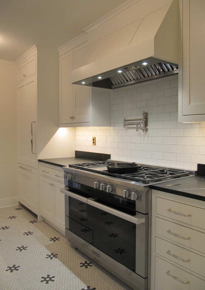 Example of a small classic galley ceramic tile and white floor enclosed kitchen design in Seattle with a farmhouse sink, recessed-panel cabinets, white cabinets, marble countertops, black backsplash, marble backsplash, paneled appliances and no island